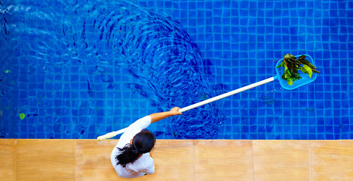 person from pool maintenance company skimming the water of a pool