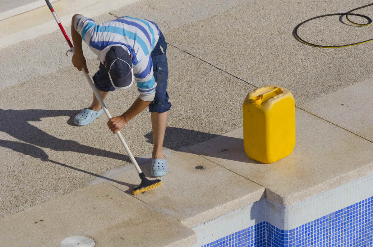 an experienced pool maintenance worker scrubbing the surfaces around the pool